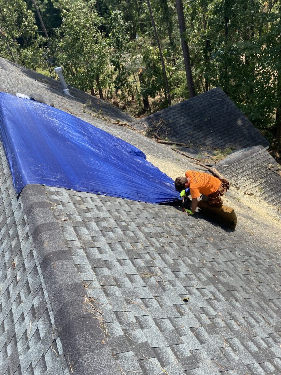 A roofer installing emergency tarping after a storm