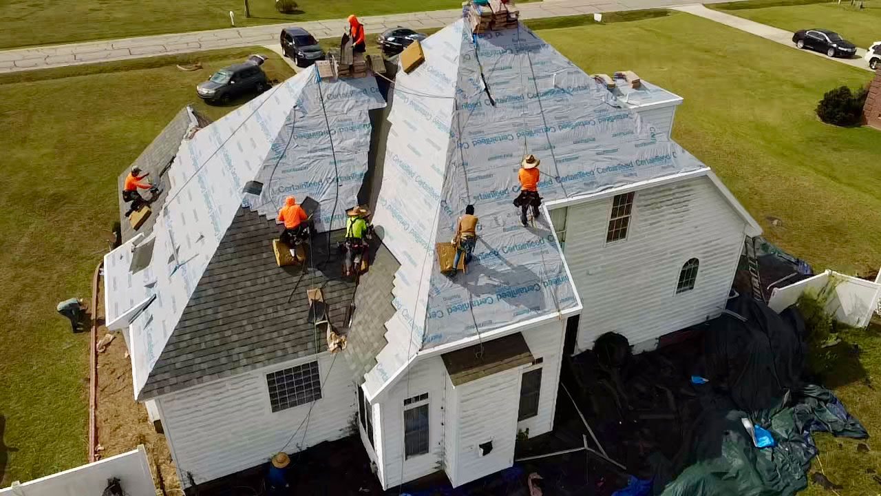 oofers working on the steep roof of a home in a grassy field on a sunny day.
