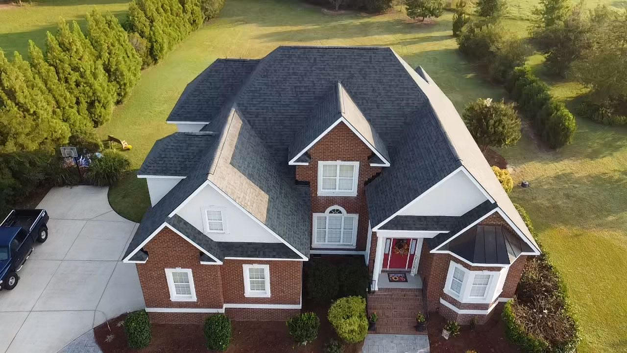 A large, stately brick home with a complex roof set into a lush, green landscape.