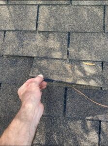 A man holding a lifted asphalt shingle