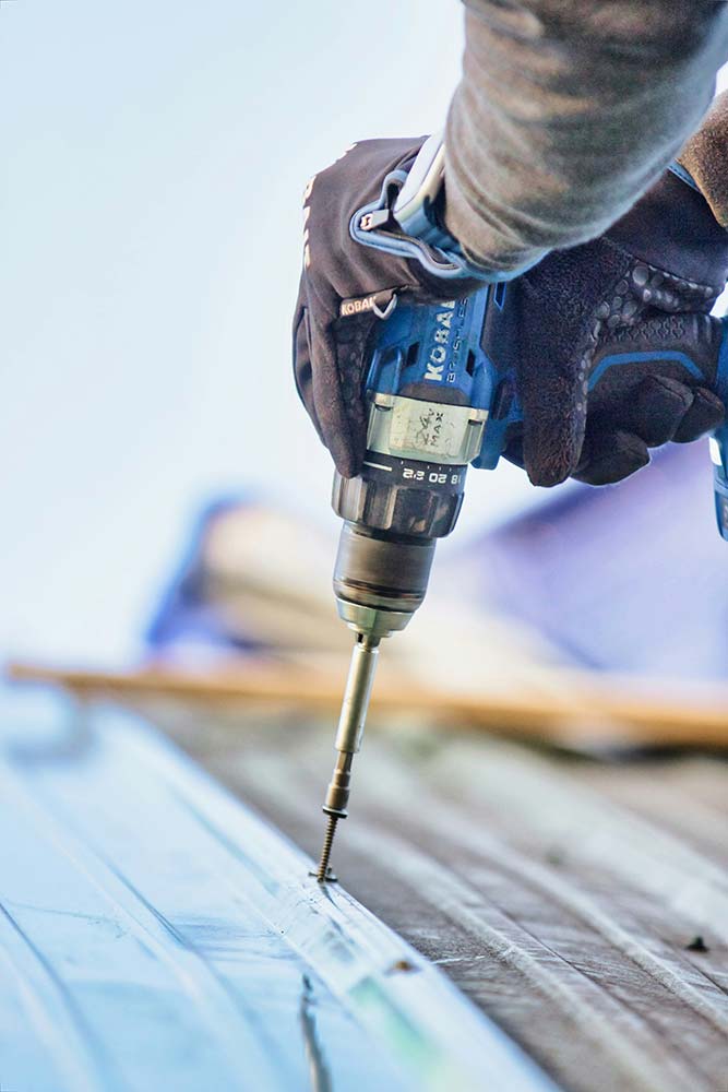 A person drilling into a metal roof